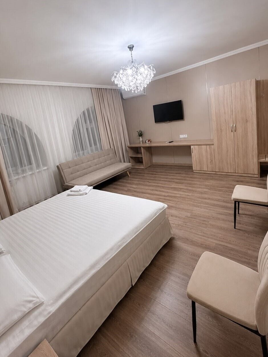 Quarto de hotel com cama, escrivaninha, cadeira, televisão e guarda-roupa.