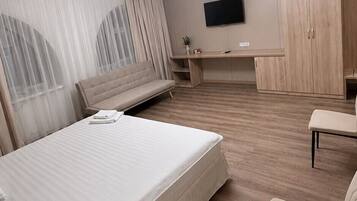 Quarto de hotel com cama, escrivaninha, cadeira, televisão e guarda-roupa.