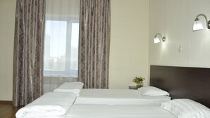 A hotel room with two beds, a nightstand with a vase of flowers, and a window with curtains. - Sultan Beibarys Hotel (Astana)