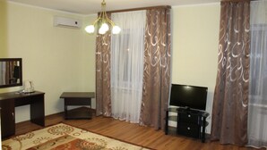 A living room with a wooden floor, a TV, a small table, and a sofa. - Sultan Beibarys Hotel (Astana)