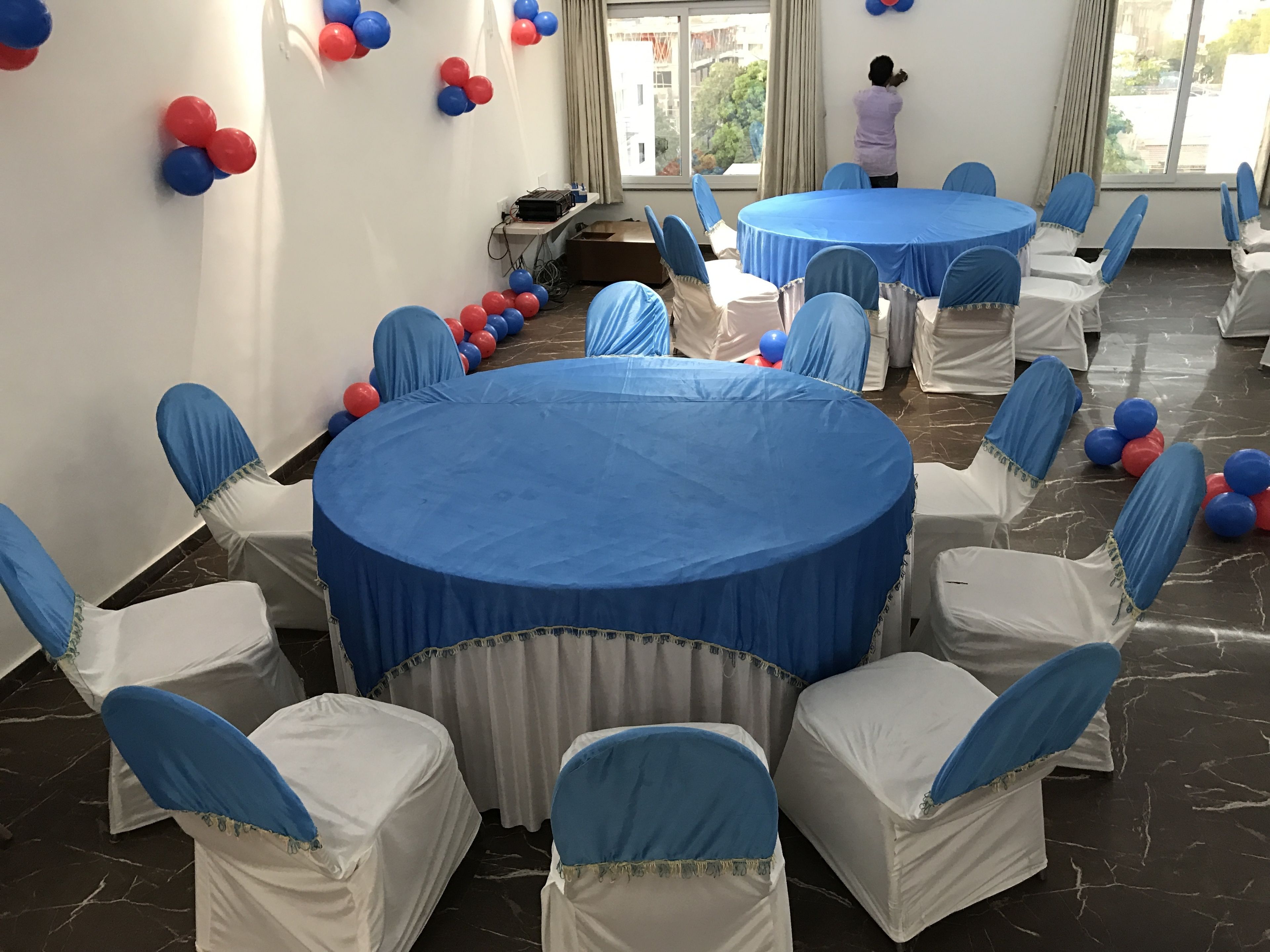 Un salón de conferencias con mesas redondas cubiertas con manteles azules, rodeado de sillas blancas con cintas azules.