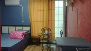 Una habitación pequeña con cama, una mesa con sillas, una ventana con cortinas y un aire acondicionado de pared.