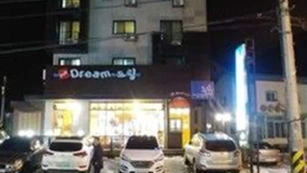 Un edificio de varios pisos con escaparate visible que dice “Dream 2J” en la noche.