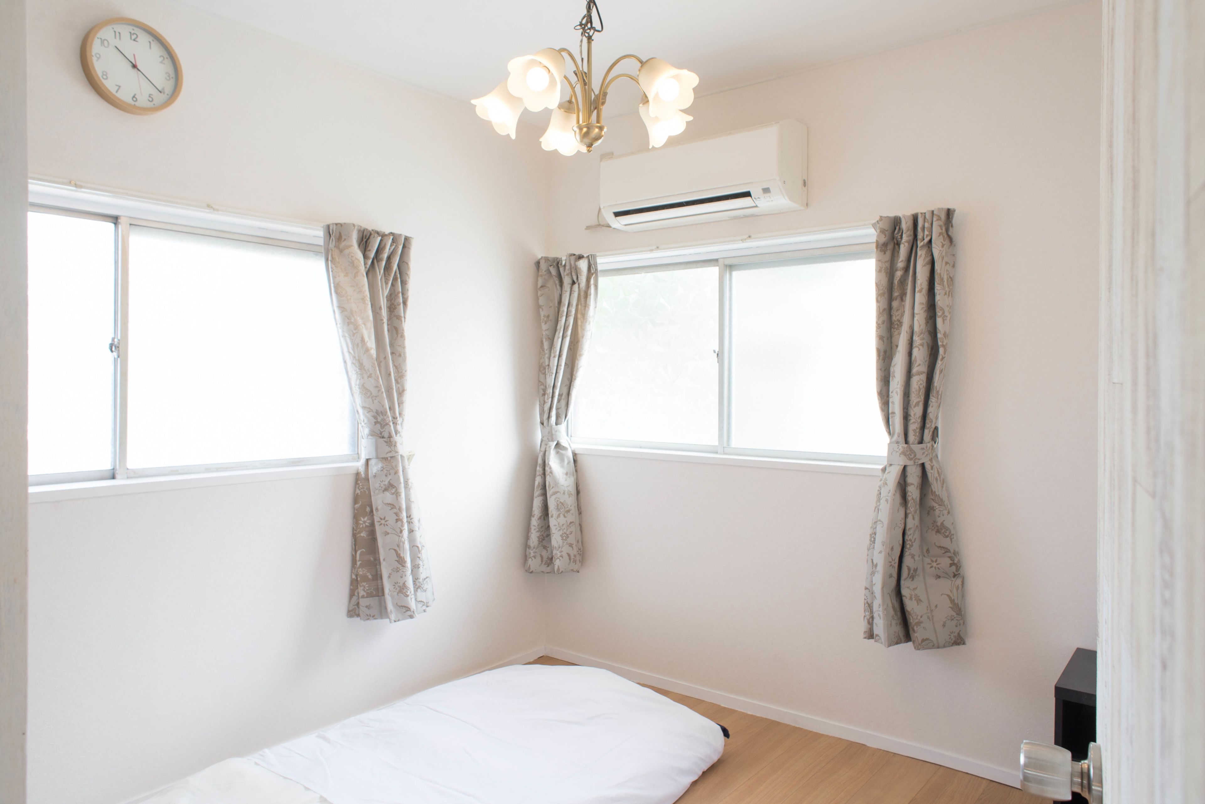 A bedroom with a bed, two windows with curtains, a ceiling light, and an air conditioning unit.