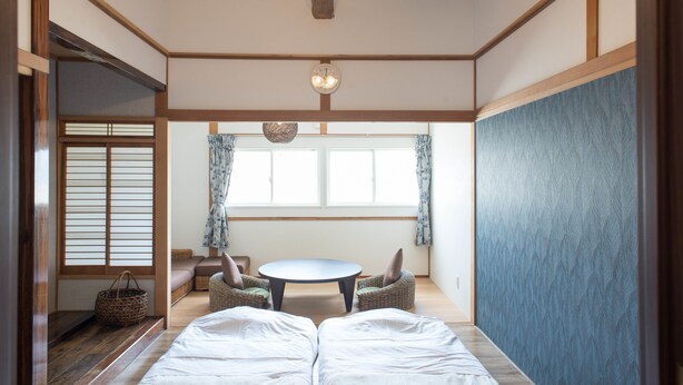 Una habitación tradicional japonesa con suelo de tatami, una mesa baja con cojines y un ventilador de techo.