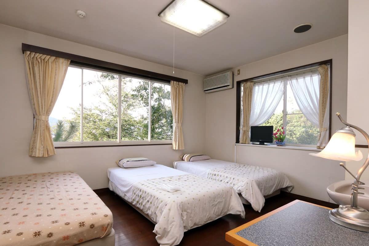A room with two single beds, a desk with a lamp, and a window with curtains.