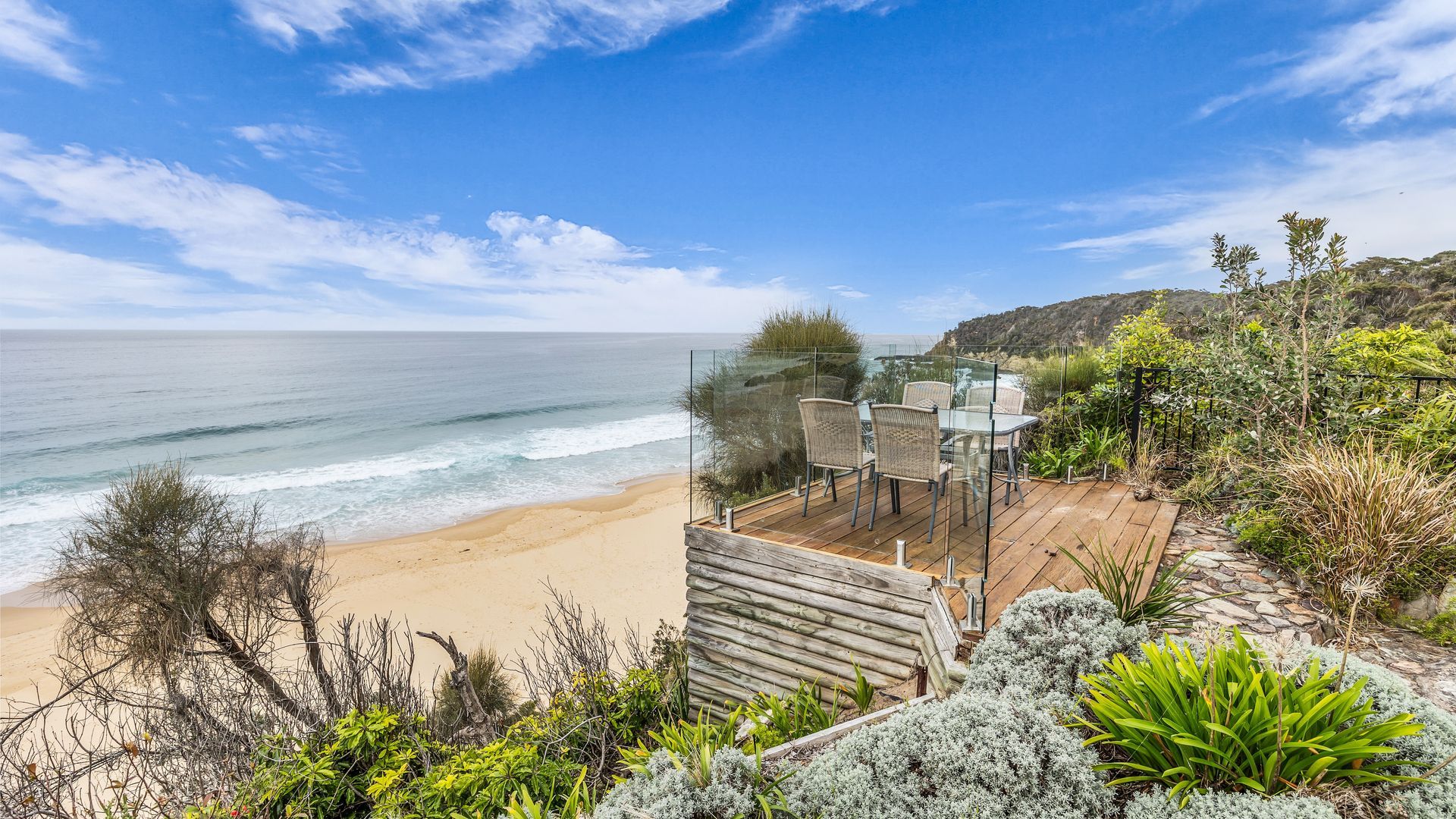 A wooden deck with glass railings overlooking a beach and ocean.