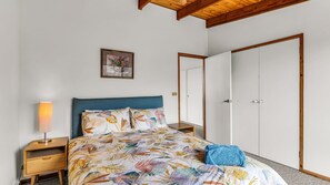 Een slaapkamer met een bed, nachtkastje, lamp, kledingkast en een lijst aan de muur.