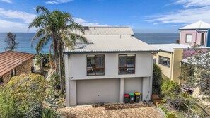 Een huis met twee verdiepingen, een garage, uitzicht op de oceaan en een palmboom.