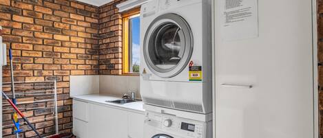 Een wasserette met een bakstenen muur, een gestapelde wasmachine en droger, een wasbak en een raam.