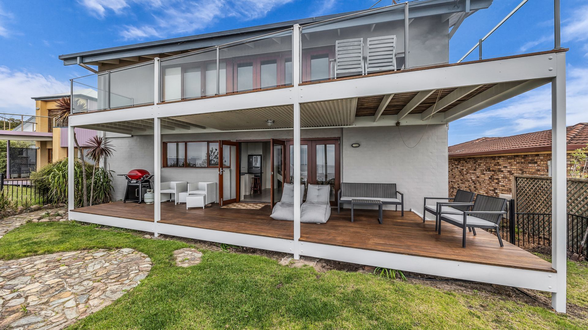 A modern two-story house with a covered patio area featuring outdoor seating and a barbecue grill.
