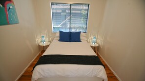A bedroom with a bed, two bedside tables, a window with blinds, and a wall with a geometric pattern.