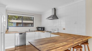 A modern kitchen with white cabinetry, a wooden countertop, a built-in stove, and a window with a view of a house.