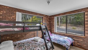Habitación con dos literas, una escalera y ventanas amplias con vistas a árboles y una carretera.