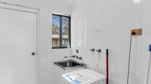 A small bathroom with white tiles, a window, a sink, and a shower.