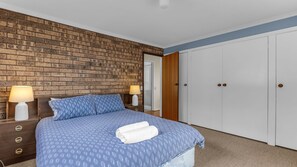 A bedroom with a brick-patterned wall, a bed with a blue patterned bedspread, two bedside lamps, and a white wardrobe.