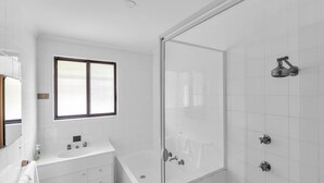 Un baño moderno con mampara de vidrio, bañera y lavamanos con ventana arriba.