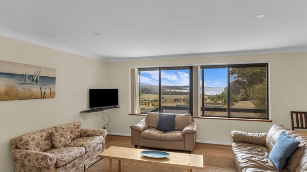 A living room with a sofa, a chair, a TV, and a view of the outdoors through large windows.