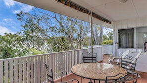 A covered outdoor patio with a round table and chairs, a white railing, and a view of trees and sky. - Lakehouse Akolele - Flower Circuit 19 (AKOLELE)