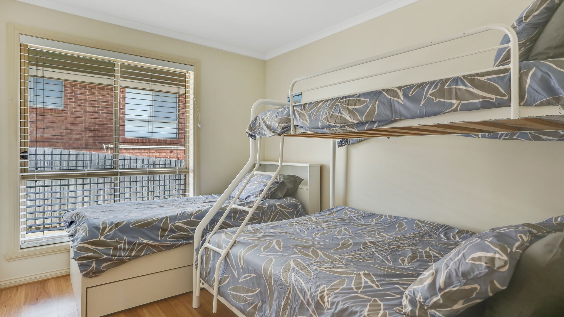 A dormitory room with bunk beds and a window overlooking a brick building.