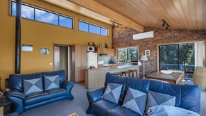 Un saló modern amb sofàs de cuir, una zona de cuina i grans finestres que donen vista a l'exterior.