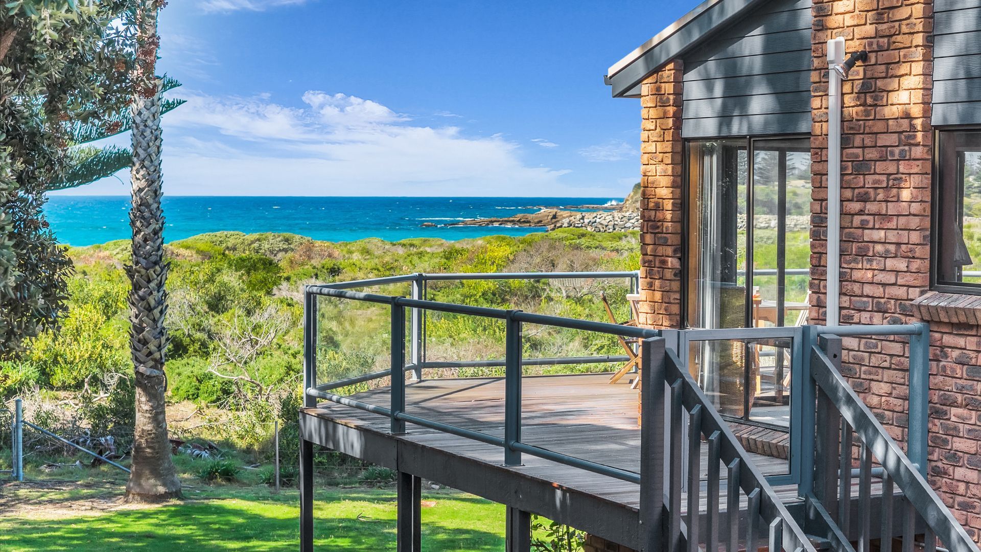 A coastal property with a deck overlooking the ocean, a brick building, and lush greenery.