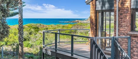 A coastal property with a deck overlooking the ocean, a brick building, and lush greenery.
