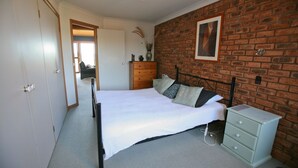 Ein Schlafzimmer mit Backsteinwand, einem Bett mit Kissen, einem Schminktisch und einer Tür zu einem anderen Raum.