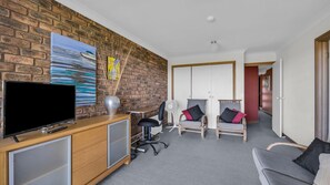 A hotel room with a brick wall, a flat-screen TV, a desk with a lamp, two chairs, and a sofa. - Breakwater 1 - Narira Street 1 (Bermagui)