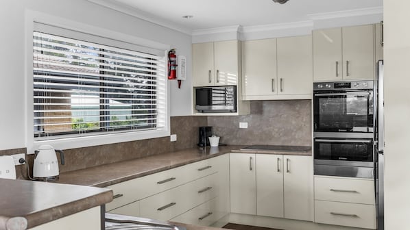 A modern kitchen with white cabinets, a built-in microwave, a double oven, and a coffee maker. - Mumbulla House - Mumbulla St 22a (BERMAGUI)