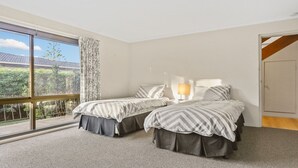 Ein Zimmer mit zwei Betten, einem Vorhangfenster, einer Lampe und Blick auf Grünfläche.