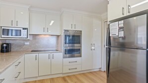 Eine moderne Küche mit weißen Schränken, einer eingebauten Mikrowelle, einem Backofen mit zwei Garstufen und einem Edelstahlkühlschrank.