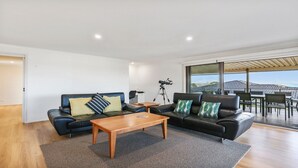 Ein modernes Wohnzimmer mit einer schwarzen Ledersofa, einem Holztisch und einem Teleskop auf einem Stativ.