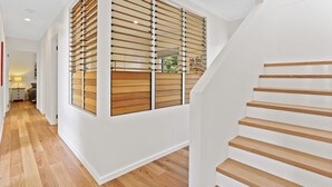 A modern interior with a wooden staircase, a hallway with a wooden floor, and a view of the outdoors through a window with wooden blinds. - Cuttagee Views - Cuttagee Beach Road 22 (BARRAGGA BAY)