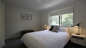 A bedroom with a large bed, two bedside tables, a window, and two wall-mounted lamps.
