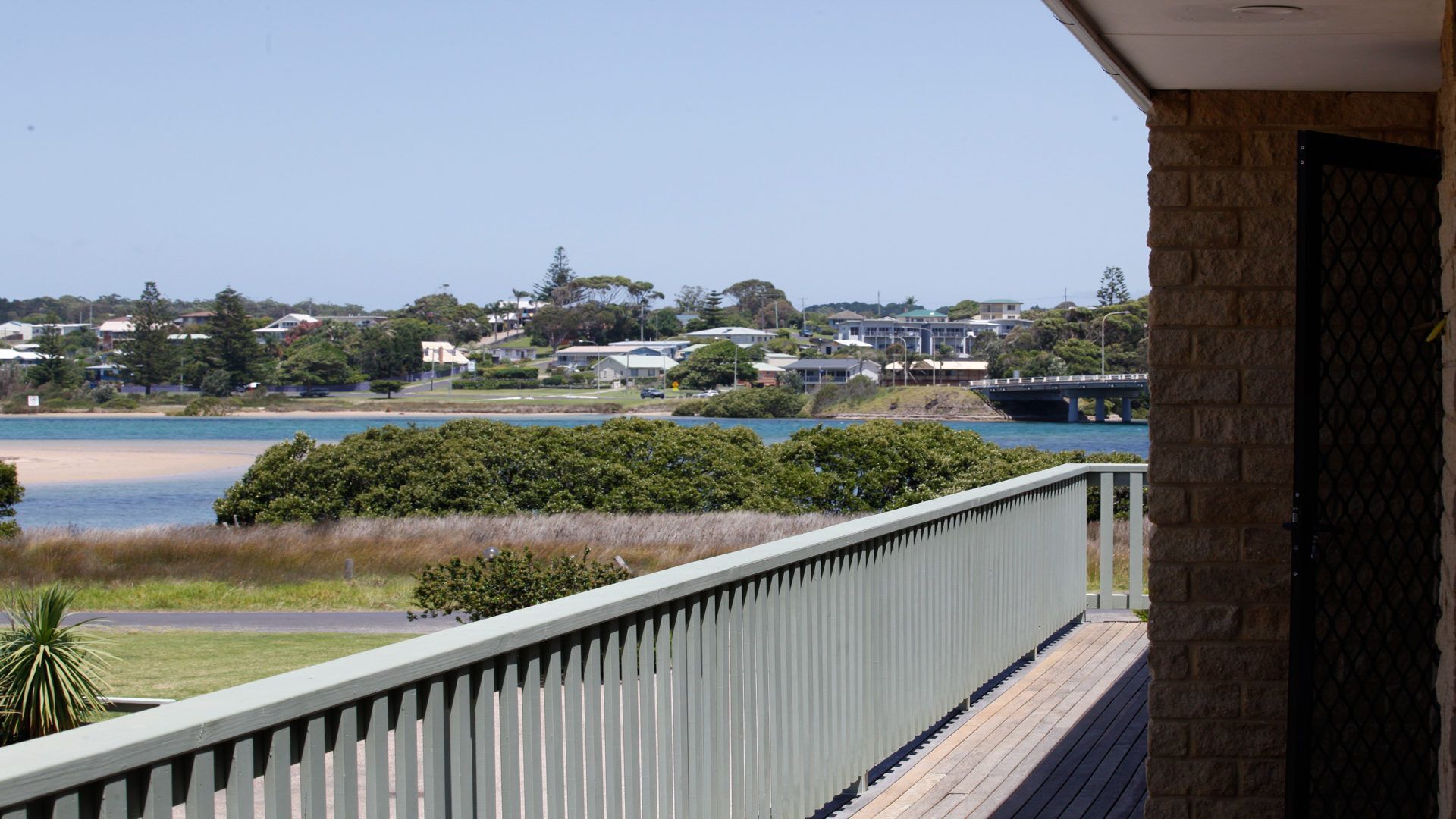 A balcony with a view of a beach, a bridge, and residential buildings.