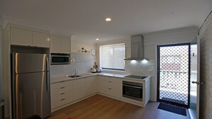 A modern kitchen with white cabinets, stainless steel appliances, a window, and a door with a security screen.