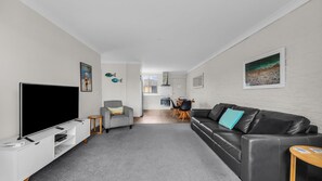 Een moderne woonkamer met een flatscreen televisie, een grijze bank, een zwarte leren hoekbank en een eethoek op de achtergrond.