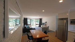 A modern kitchen with a built-in oven and microwave, a dining area with a wooden table and chairs, and a living area with a sofa and a TV.