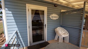 Une véranda couverte avec une porte-fenêtre coulissante, une enseigne indiquant « Hébergement de vacances à ABERDEEN », et une chaise en plastique blanche.