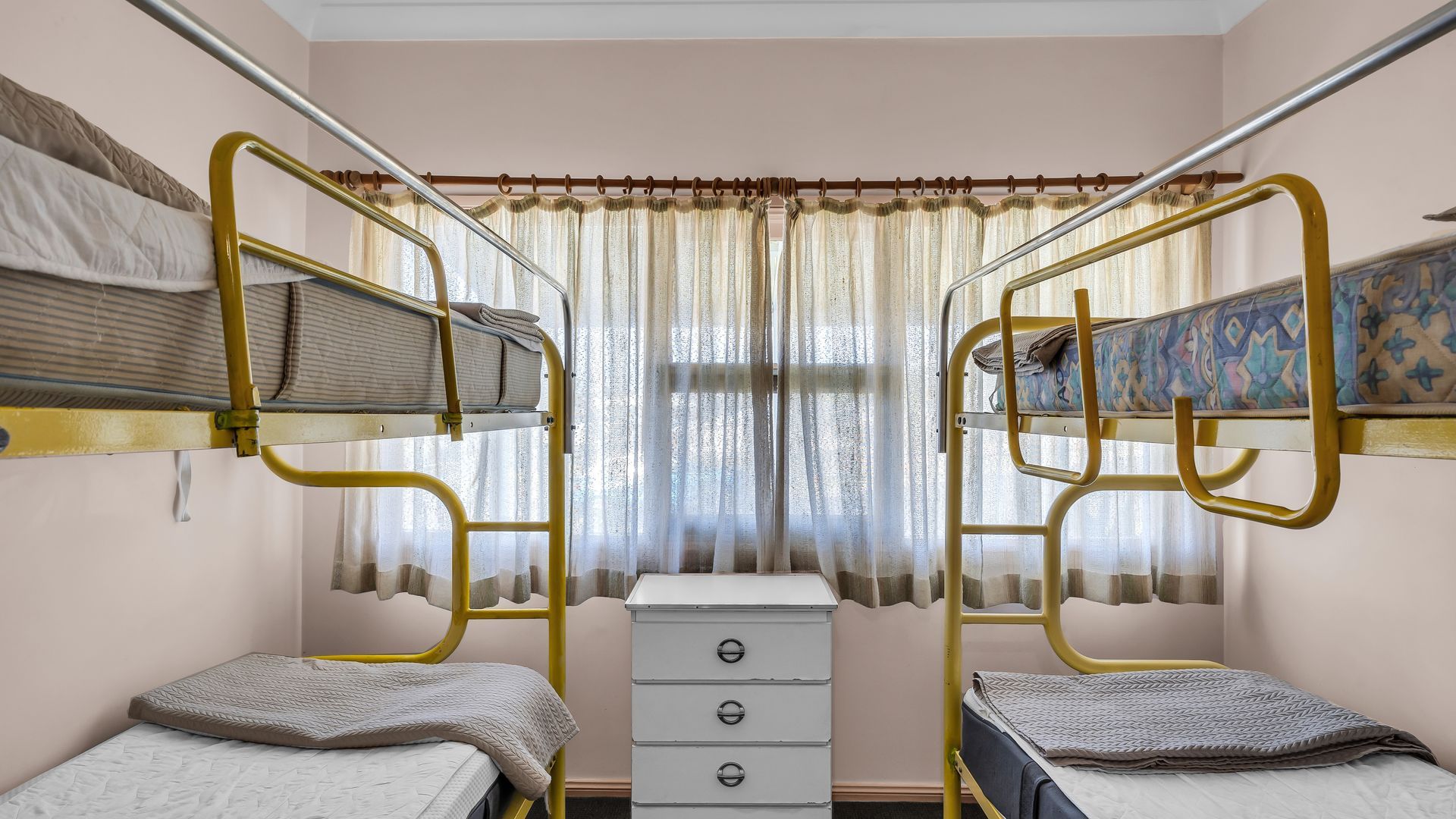 A bunk bed room with a small white dresser and a window with curtains.