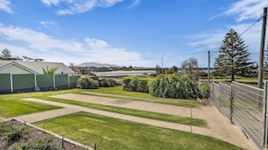 A residential backyard with a lawn, a paved patio, and a view of a beach and mountains in the distance.