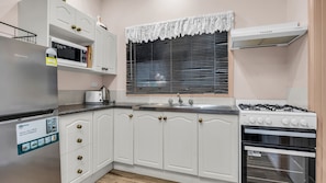A kitchen with white cabinetry, a stainless steel refrigerator, a microwave, a stove, and a window with blinds.