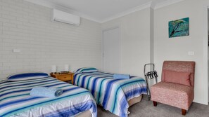 A bedroom with two beds, a chair, a nightstand, and a wall-mounted air conditioner.
