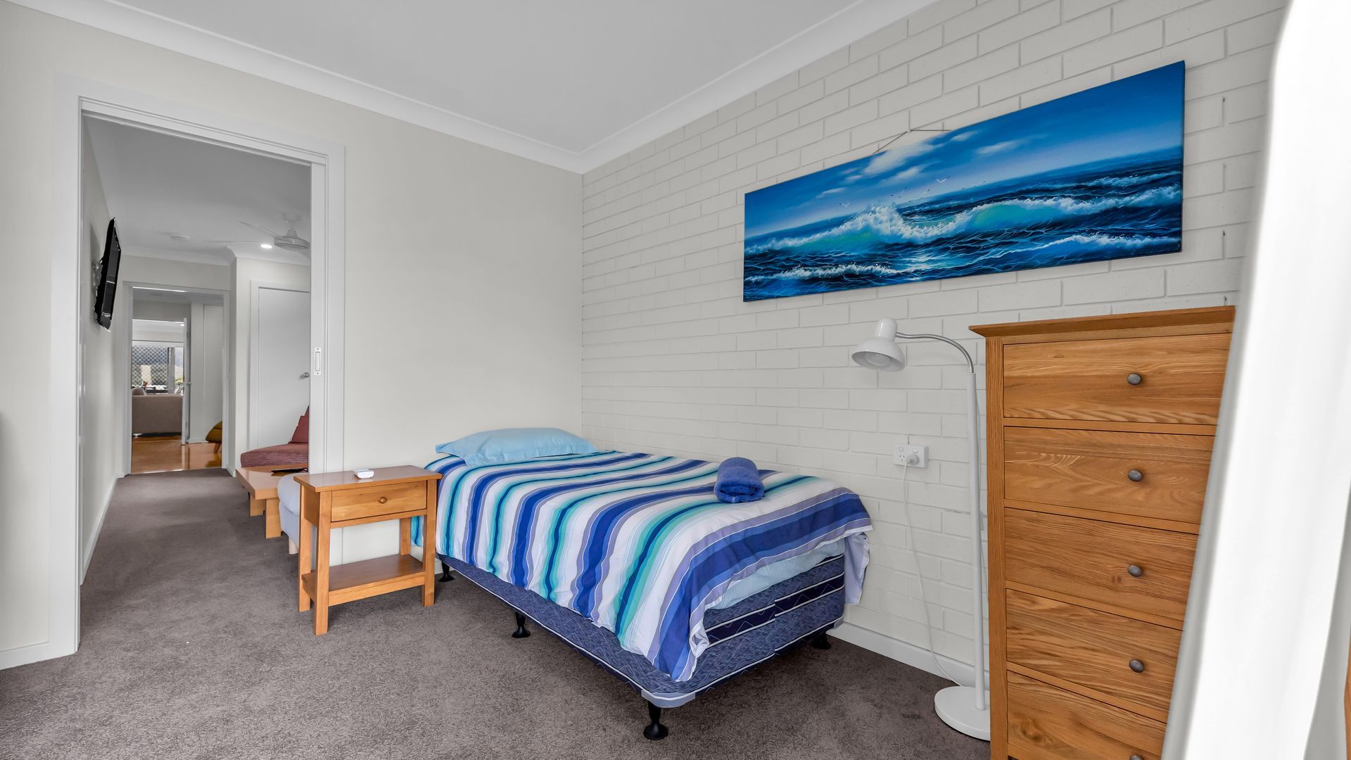 Een slaapkamer met een bed, een houten dressoir, een bureau, een stoel en een schilderij van de zee aan de muur.