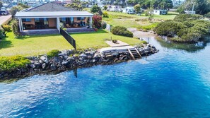 A house with a covered patio, a swimming pool, and a rocky shoreline.