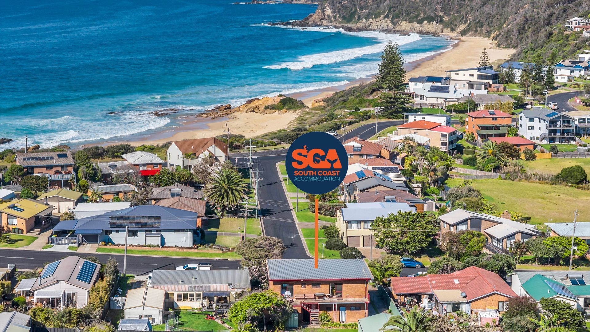 A coastal residential area with houses, a road, and a beach.