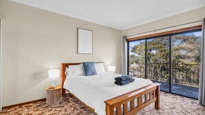 Une chambre à coucher avec un grand lit, une table de chevet, une lampe, un banc et un balcon donnant sur la forêt.