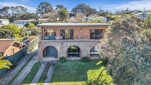 Une maison à deux étages avec une façade en briques, un balcon doté d’un espace salon extérieur et une pelouse bien entretenue.