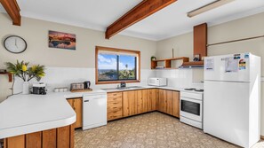 A kitchen with wooden cabinets, a white countertop, a built-in oven, a microwave, and a refrigerator. - Beares Beach House - Mill Street 7 (BERMAGUI)